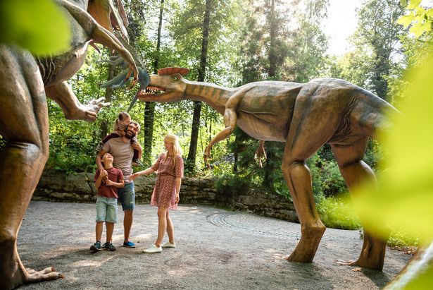 Eine Familie bestaunt zwei Dinosaurier in Originalgröße. Sie stehen im Saurierpark.