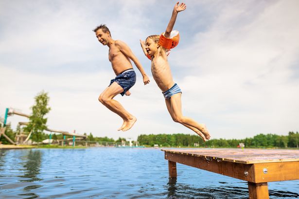 Junge und Vater springen in den See. Im Hintergrund ist eine Wasserrutsche zu sehen.